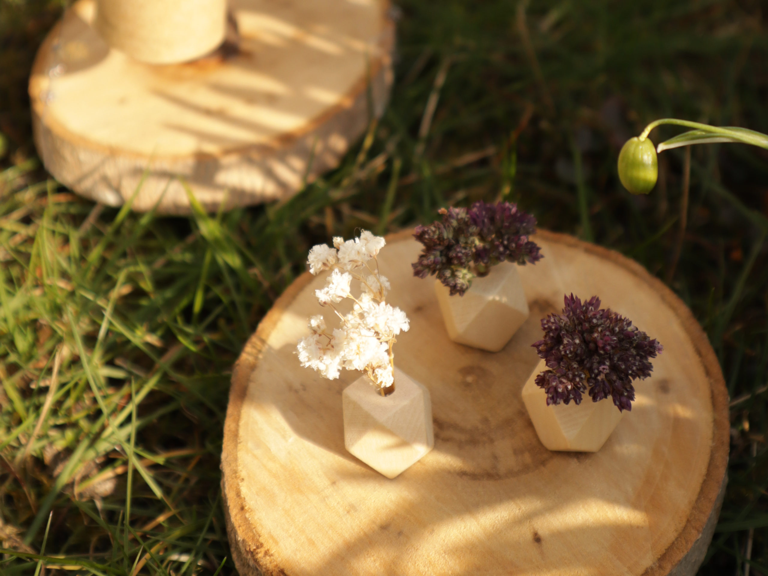Drei kleine Blumenvasen: 
Auf einer zweiten Baumscheibe stehen drei eckige Holzperlen, in die kleine getrocknete Blumen gesteckt sind. 