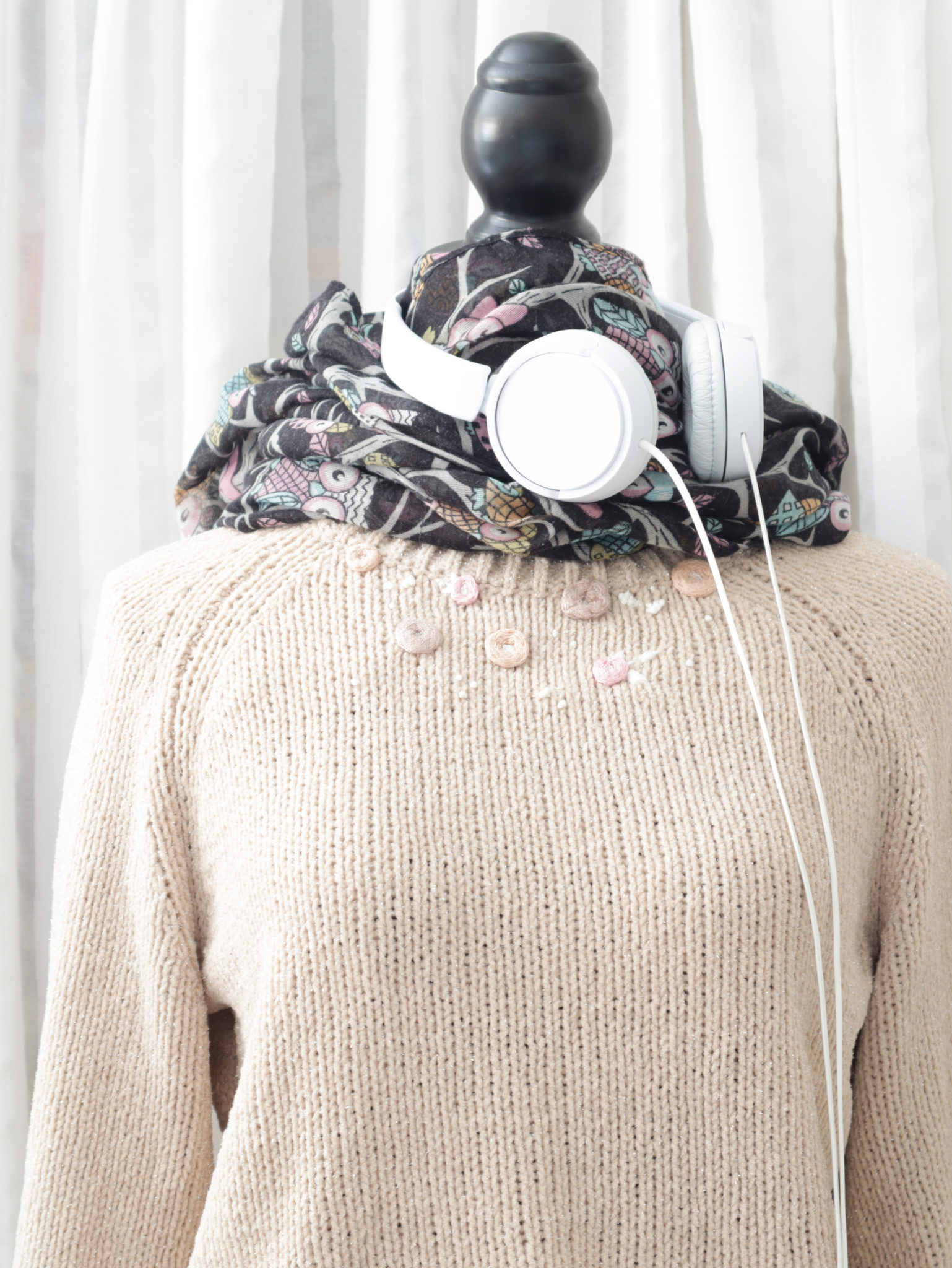 Bestickter Pullover auf einer Anziehpuppe mit Schal und Kopfhörern.