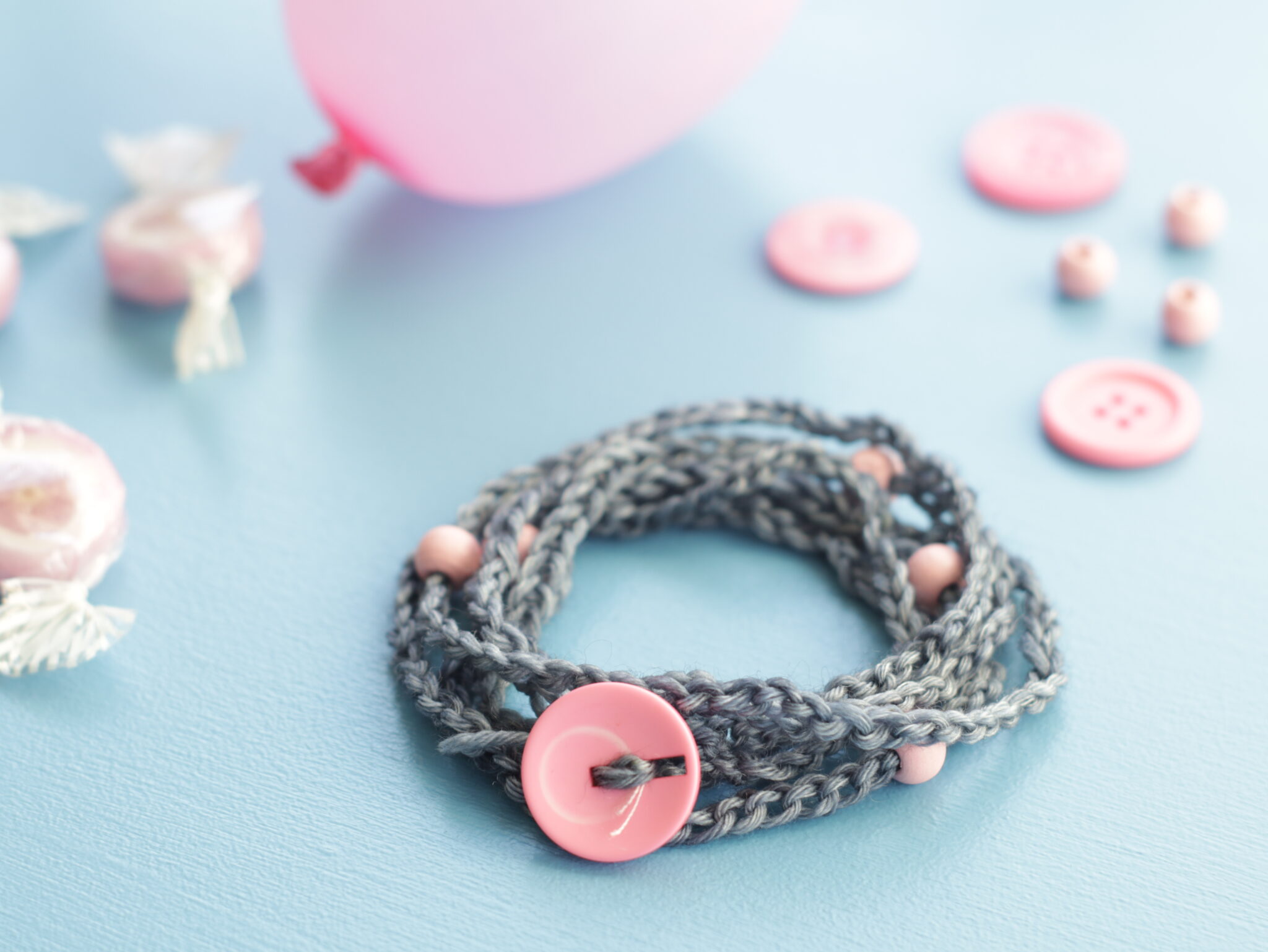 Gehäkeltes graues Armband mit rosa Knopf und rosa Perlen.