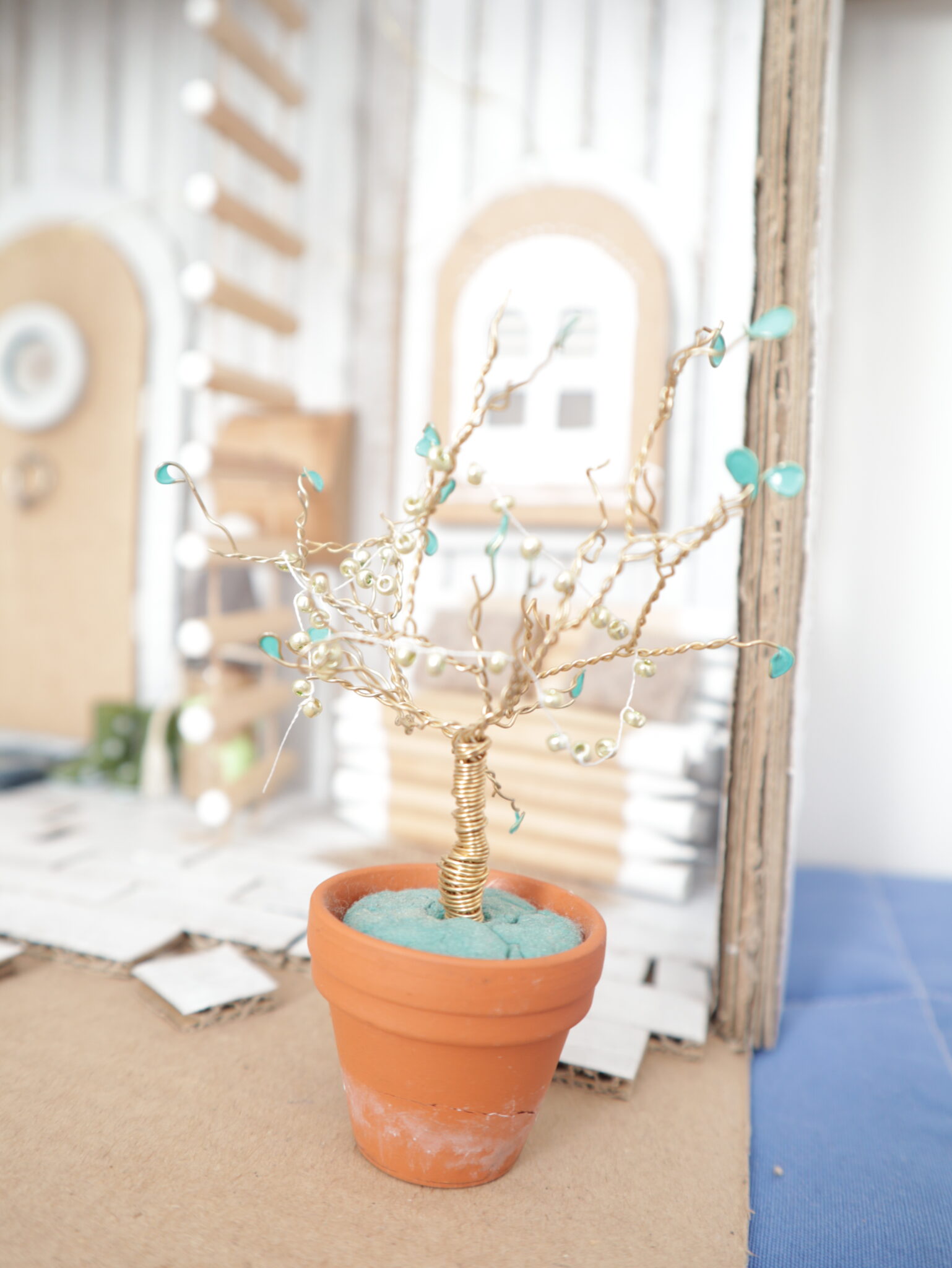 Dekoratives Gartenelement: Drahtbaum mit türkisen Blüten im Mini-Terrakotta-Blumentopf.