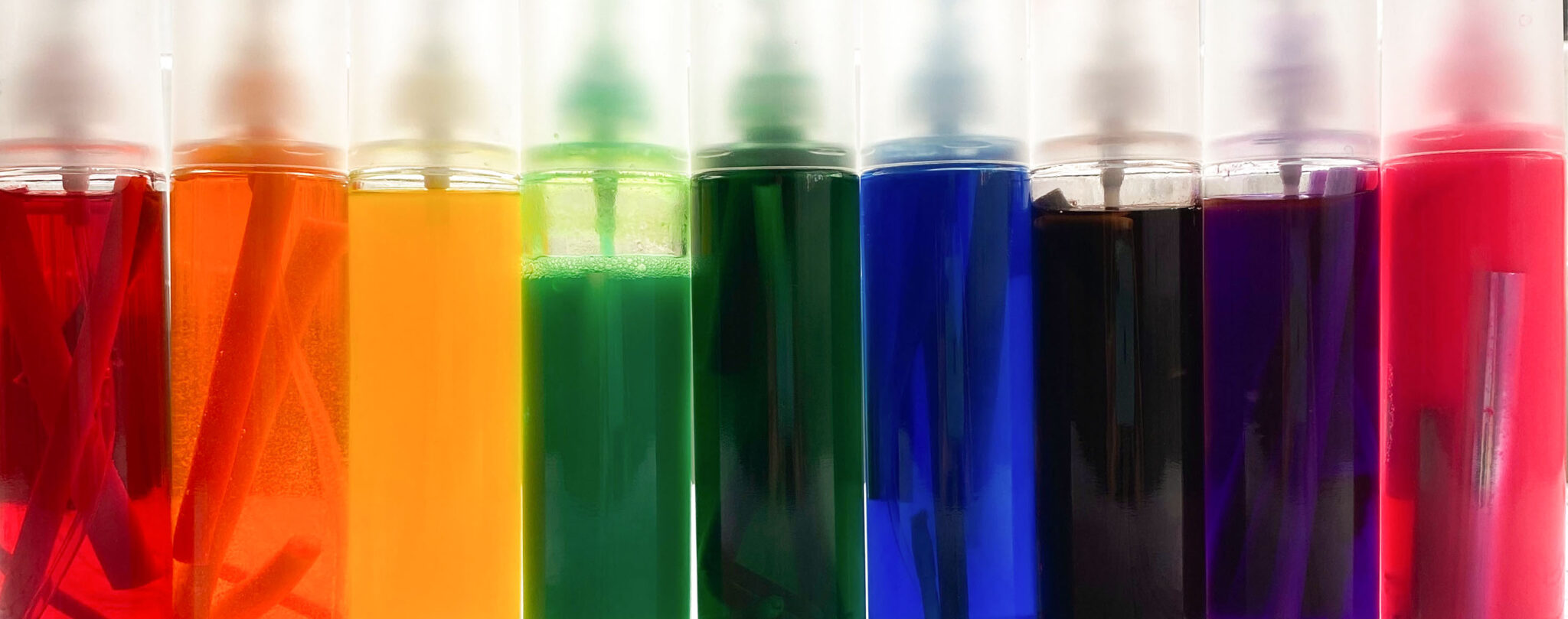 Glas-Sprühflaschen in einer Reihe stehend, mit flüssiger Farbe darin. Diese Farbe stammt aus leeren oder eingetrockneten Filzstiften.